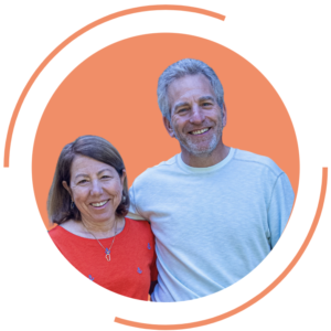 A circular image of a Debra Meyerson and Steve Zuckerman against an orange background. The woman on the left has brown hair and wears a red top with a necklace. The man on the right has gray hair and a beard, wearing a white t-shirt. They are standing close together. The circular image is framed by a partial orange circular border.